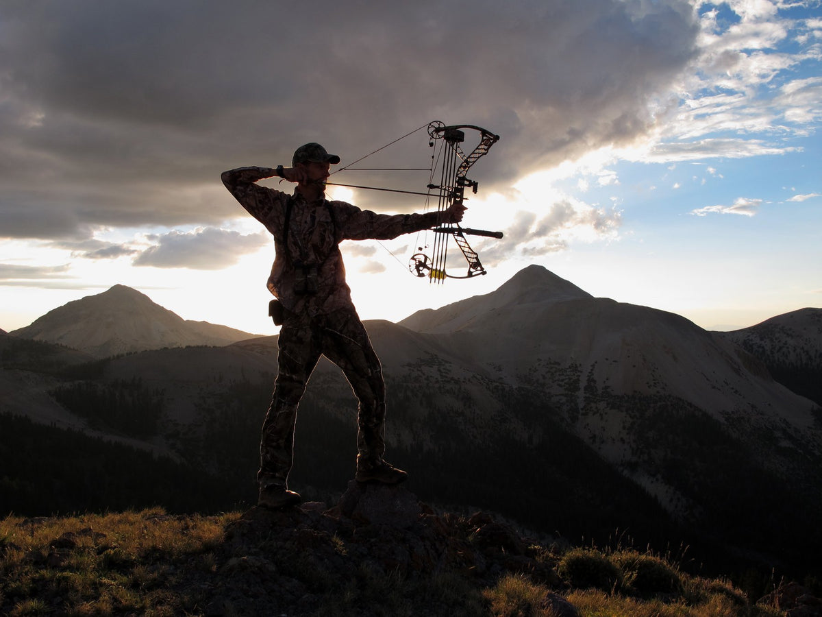 Bowhunter at full draw silhouetted on a mountain ridge at sunset