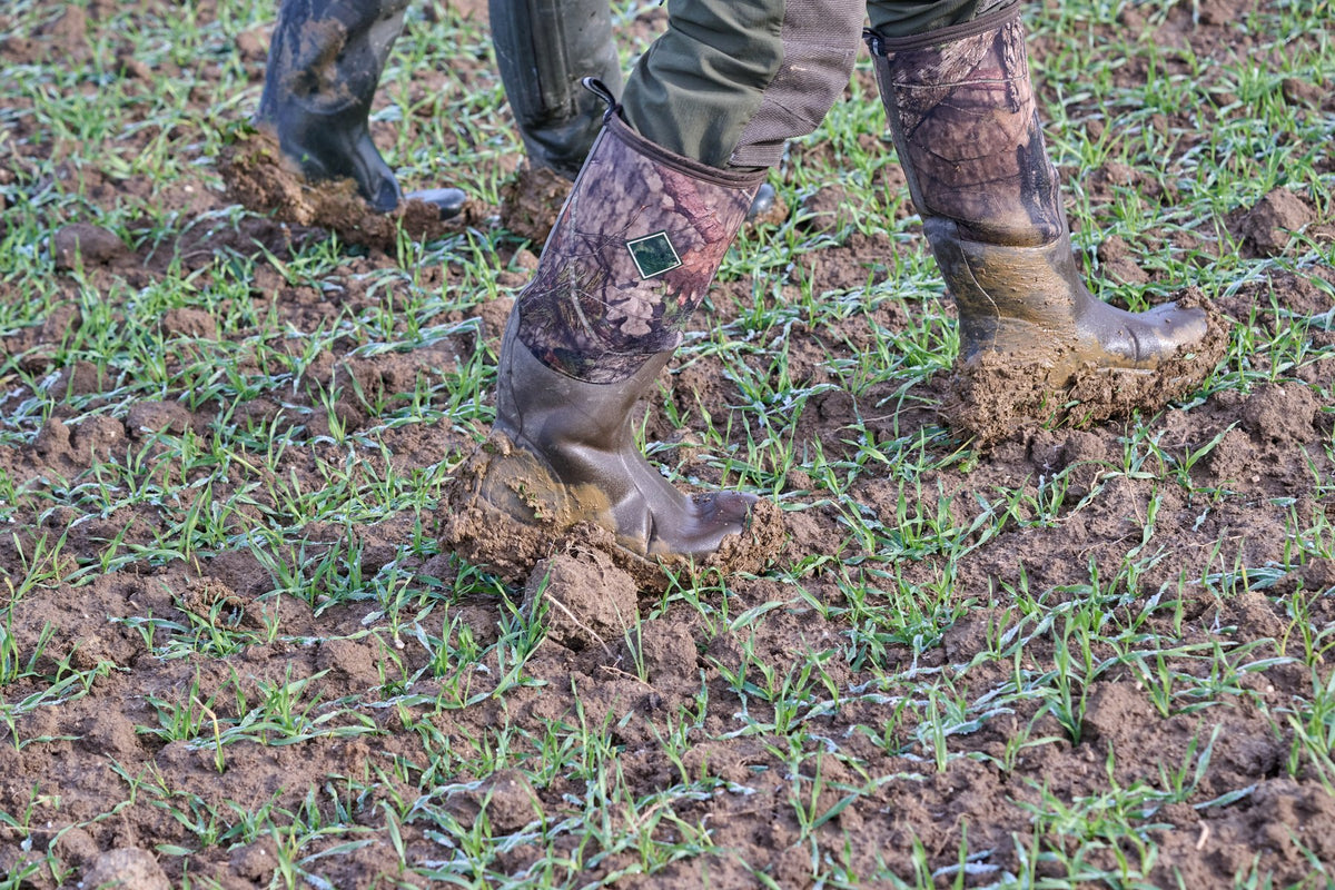 Hunter walking through a muddy field in camo rubber hunting boots