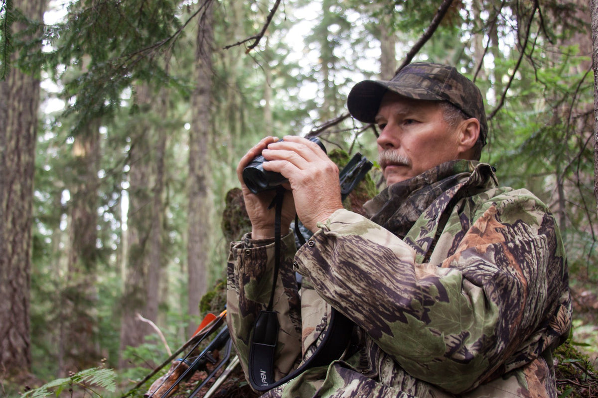 Bowhunter in camo glassing a timbered hillside with binoculars